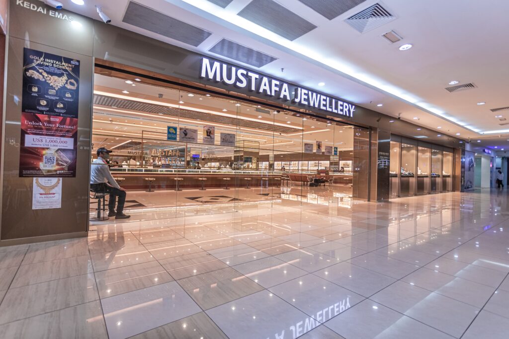 captures the wide, modern storefront of "Mustafa Jewellery," located inside a well-lit shopping mall or commercial complex. The storefront features an expansive glass facade that offers a clear, open view into the spacious interior of the showroom.